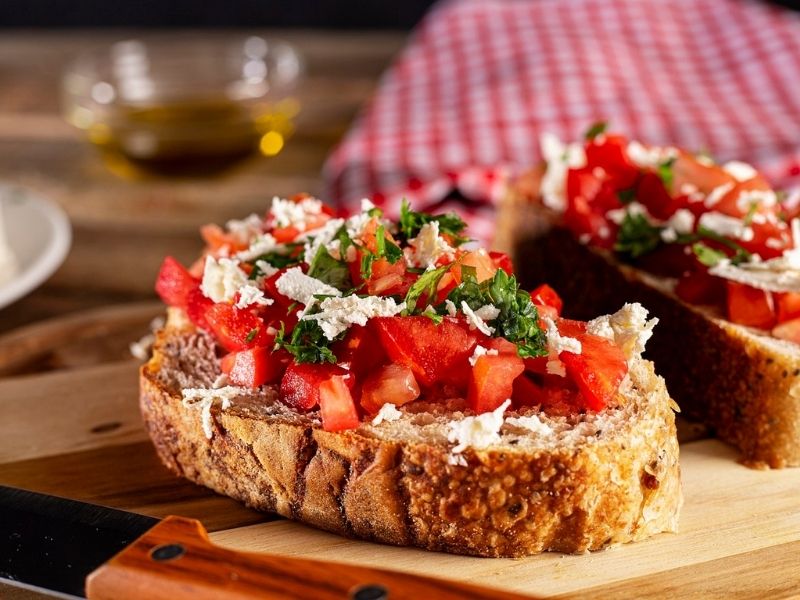 Bruschetta snack with grilled bread, fresh tomatoes, basil, olive oil and mozzarella on a wooden board – a crispy and fresh flavor combination from Italy.