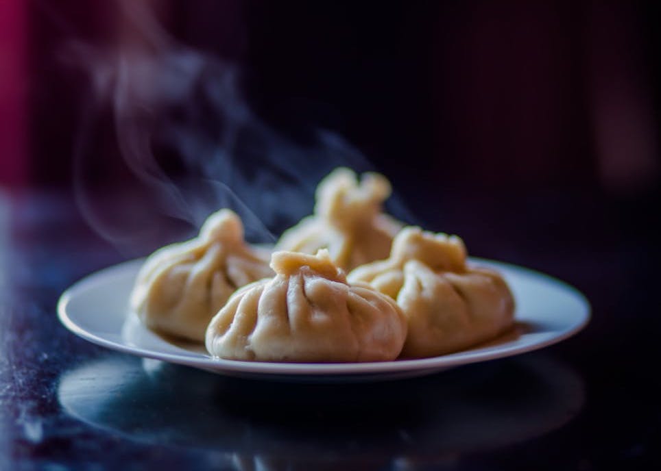 Dim sum dumplings filled with chicken, shrimp, and vegetables, served hot steamed in a white ceramic plate – a classic Chinese snack.